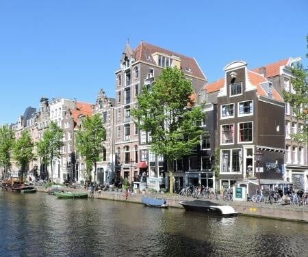 Maisons de maître le long des canaux d'Amsterdam avec des bateaux amarrés au quai par une journée ensoleillée.